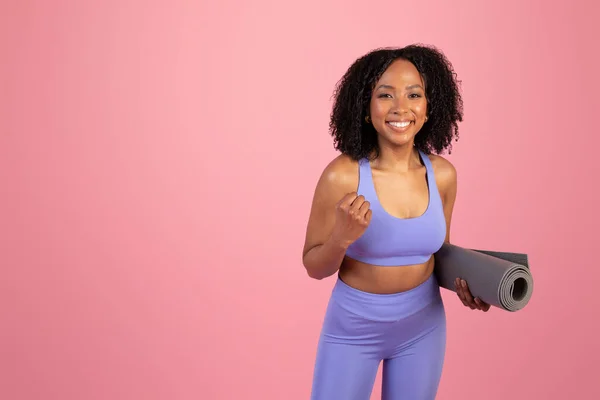 スポーツウェア作りの成功を祝う マットを保持し ピンクのスタジオの背景に一人でスポーツを楽しむスポーツウェアの若いアフリカ系アメリカ人女性 フィットライフスタイル 広告やオファー ボディケア ワークアウト — ストック写真