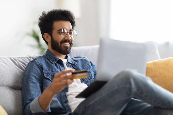 Усміхнений Індійський Чоловік Окулярах Використовуючи Ноутбук Кредитну Картку Вдома Онлайн — стокове фото