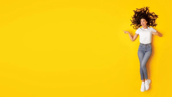 広告を提供します 興奮した女は黄色の背景の上に横たわるテキストのためのフリースペースで脇に指を指して 若い女性の広告何かがコピースペースを示す トップ表示 — ストック写真