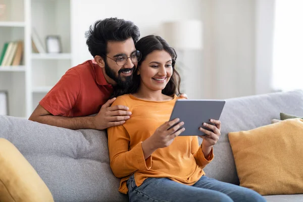 Mutlu Doğu Eşleri 'nin portresi evde dijital tabletle rahatlıyor, gülümseyen Hintli genç bir çift modern Gadget ile koltukta dinleniyor, internete ya da alışverişe bakıyor, kopyalama alanı kullanıyor.