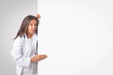 Sıhhatin artması. Tıbbî reklamlar için boş pano sergileyen kıdemli kadın doktor, ücretsiz fotokopi alanı ile maket yapıyor.