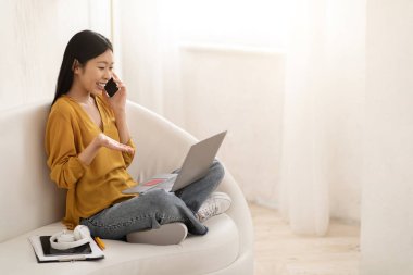 Evdeki kanepede oturmuş, dizüstü bilgisayar, banka kartı kullanarak, telefonla konuşarak müşteri hizmetleri temsilcisiyle, internetten alışveriş yaparak, fotokopi çekerek mutlu bir Asyalı kadın.