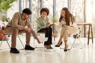 Şirket Toplantısı. Üç çok ırklı meslektaştan oluşan bir ekip, yeni iş projesini konuşuyor. Zeminde oturan kağıtlara bakıyorlar ve modern ofiste beyin fırtınası yapıyorlar. Takım Çalışması Konsepti
