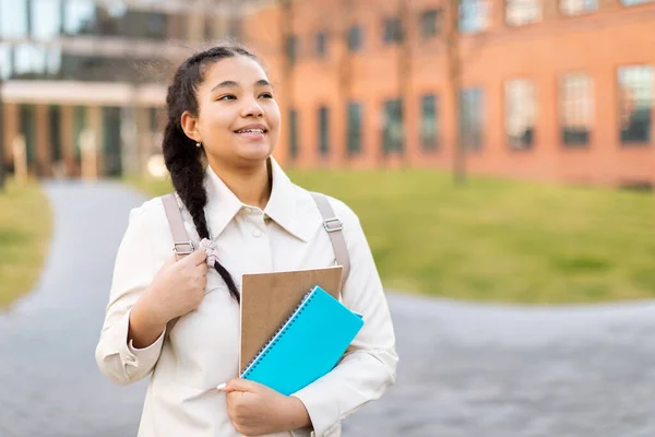 一个积极的女学生站在室外 带着练习本和背包在大学校园里散步 面带微笑的形象 自由自在的空间 — 图库照片