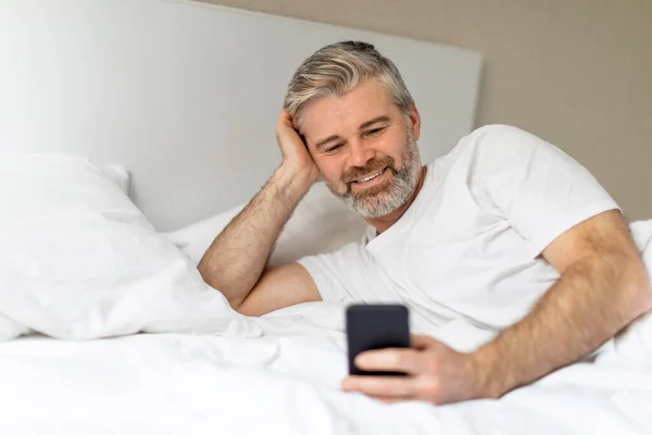 Счастливый Красивый Седой Европейский Мужчина Средних Лет Лежал Постели Телефоном — стоковое фото