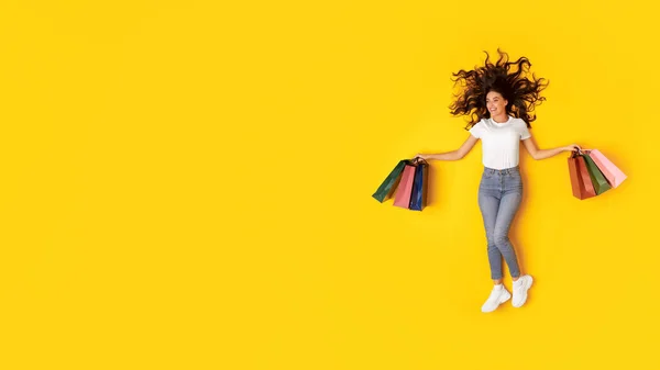 销售报价 一个女人提着购物袋往外看在黄色工作室背景上的复制空间 快乐女士广告季节性折扣持有许多纸袋购物者 — 图库照片