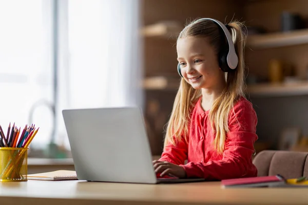 Web-Based Education. Cute Little Schoolgirl Wearing Wireless Headphones Study With Laptop At Home, Smiling Preteen Female Child Sitting At Desk And Using Computer For Online Lesson, Copy Space