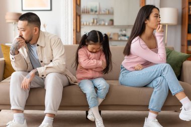 Aile kavgası. Japon anne babalar ve kızıyla birlikte üzgün bir şekilde oturan gergin bir çatışma sonrası depresyona giren, evdeki koltukta gergin bir an pozu veren. Çatışmalar ve Mutsuzluk Problemi