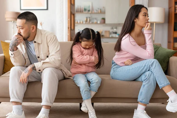 Family Struggles. Upset Japanese Parents And Daughter Sitting With Sadly Bowed Heads Depressed After Intense Conflict, Having Tense Moment Posing On Couch At Home. Conflicts And Unhappiness Problem