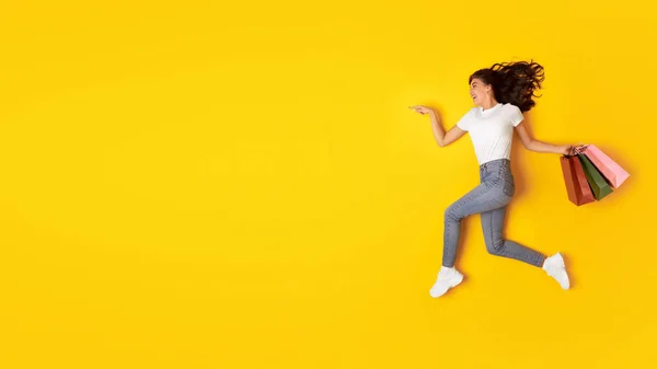 哇销售 快乐的女人在黄色工作室的背景下 用购物袋做广告 用手指在空旷的地方做广告 时尚与商业 — 图库照片