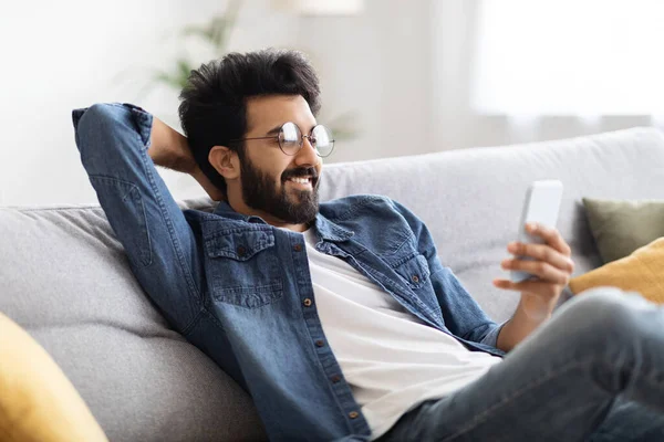 Smiling Millenniing Indian Guy Messages Smartphone While Relaxing Home Happy — 스톡 사진