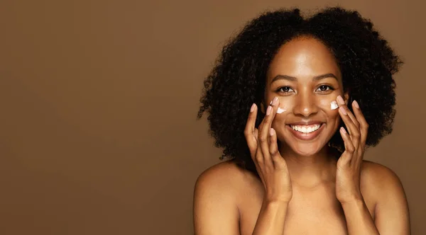 スキンケア 明るく魅力的なトップレスアフリカ系アメリカ人の100万人の女性が顔を指でマッサージし カメラで笑顔を撮影し クリームを適用し 茶色に隔離され コピースペース — ストック写真