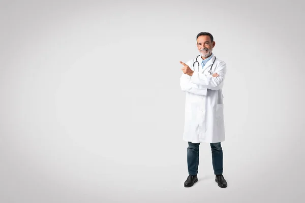 Cheerful European Senior Man Doctor White Coat Stethoscope Points Finger — Fotografia de Stock