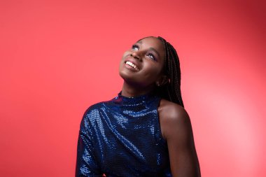 Sequin Party 'deki hayalperest genç siyah kadın fotokopi odasına bakıyor mutlu gülümseyen, sanatçı makyajlı ve kırmızı arka planda piercing pozu veren güzel Afrikalı Amerikalı kadın.