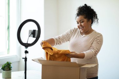 Moda etkisinde olan mutlu, tombul, İspanyol bir kadın. Kağıt kutudan yeni bir bez çıkarıyor ve gülümsüyor. Web mağazası tavsiye ediyor.