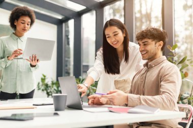 Takım çalışması ve birlik. Dizüstü bilgisayarda birlikte çalışan üç genç uzmandan oluşan profesyonel iş ekibi, Ofisteki Şirket İşbirliği yoluyla verimliliği artırıyor.