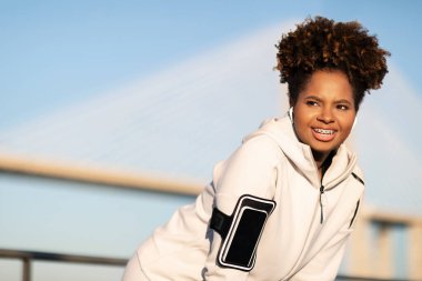 Siyah kadın koşucu dışarıda antrenman yaptıktan sonra dinlenmek için duruyor, Kol bandı takmış gülümseyen genç Afrikalı Amerikalı kadın açık havada koştuktan sonra nefes alıyor, yakın çekim, kopyalama alanı