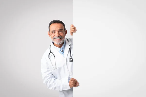 灰色の背景にコピースペースと大きなバナー付き聴診器付き白いコートで積極的に面白いヨーロッパの高齢者の医師 専門家の勧告 広告やオファー — ストック写真