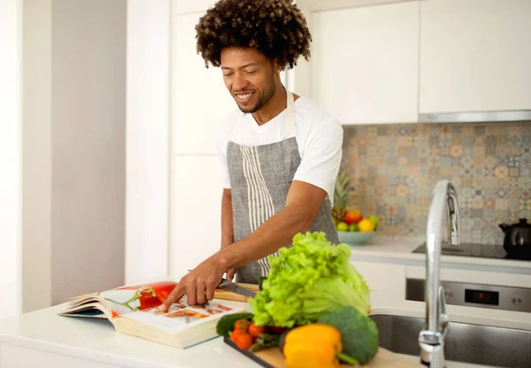 요리에 Happy Black Man Cooking Using Traditional Paper Recipe Book — 스톡 사진
