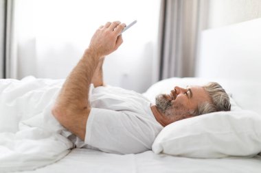 Gadgets bağımlılık konsepti. Mutlu gülümseyen orta yaşlı bir adamın evde telefonu kullanması uyandıktan sonra kız arkadaşına mesaj atması e-postaları kontrol etmesi, fotokopi çekmesi.