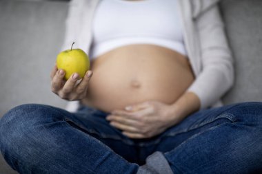 Doğum öncesi diyeti. Yeşil Elma Tutan Genç Hamile Kadın 'ın Kesilmiş Görüntüsü ve Dokunaklı Belly, Tanınmayan Beklenmeyen Anne Vitamin Meyvesinin tadını Çıkartıyor, Hamilelik sırasında Sağlıklı Beslenmeyi Seçiyor