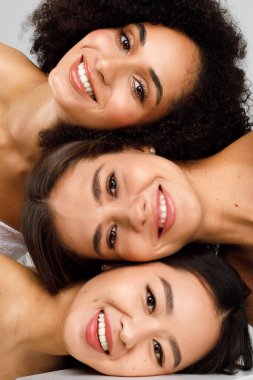 Yüzü mükemmel şekilde parlayan üç farklı kadın birlikte poz veriyor ve gülümsüyor, dikey stüdyo çekimi, yakın çekim. Çok kültürlü güzellik kavramı