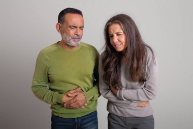 Mutsuz Kafkasyalı yaşlı adam ve bayan gri stüdyo arka planında mide ve çan ağrısından muzdarip. Zehirlenme, ishal, pankreas iltihabı, mide ekşimesi ve sağlık sorunları, ülser