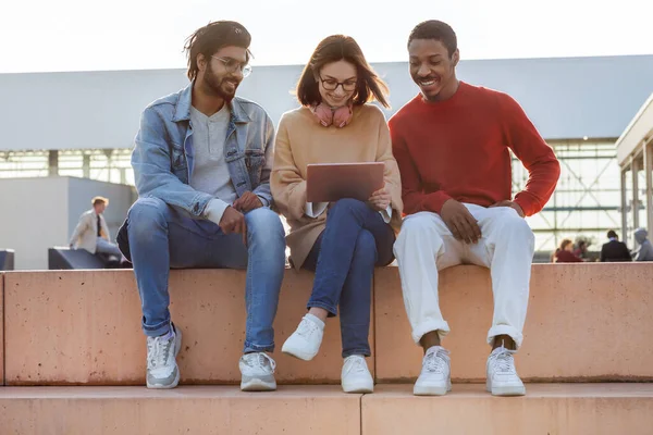 stock image Cheerful black, arab and european millennial students watching online lesson on tablet in campus, outdoor. Break, education, knowledge and communication, study at university