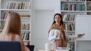 Etkileşimli öğrenme. Profesyonel genç bayan öğretmen sınıftaki beyaz tahtanın yanında duran öğrencilere yeni konuyu açıklıyor, bir kız soru sormak için elini kaldırıyor, çekim takibi, yavaş çekim