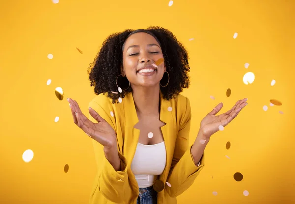 Festive mood. Excited pretty black lady throwing confetti, celebrating holiday isolated on yellow background, studio shot. Ad and offer for huge party, New Year