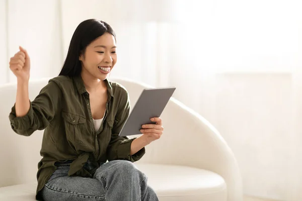 長い絹のような髪を持つ感情的にかわいい魅力的な韓国の女性は デジタルタブレットでソファに座って パッド画面とジェスチャーを見て オンライン取引やギャンブル ホームインテリア コピースペース — ストック写真