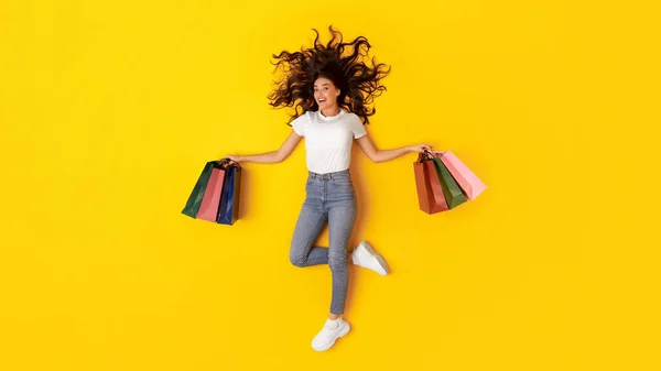 购物及售卖优惠广告 快乐的女士握着许多纸袋 躺在黄色的背景上 微笑着拍照 全长拍摄的购物狂女人 顶视图 — 图库照片