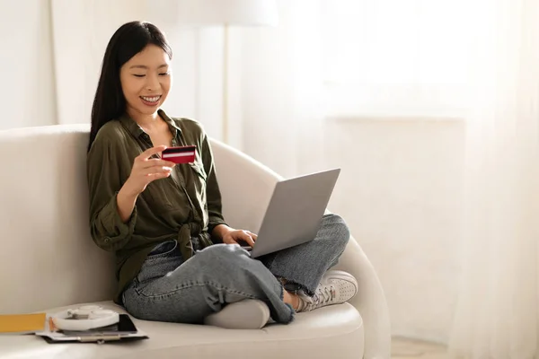 明るい魅力的な若いアジアの女性の独立した請負業者の笑顔ソファに座って 自宅で現代のPcのラップトップと銀行カードを使用して インターネット上の商品やサービスの支払い スペースのコピー — ストック写真