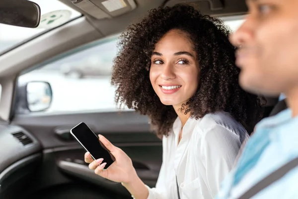 助手席に座って運転席の男を見ている車の中でスマートフォンを持っている陽気な中東の女性 交通とナビゲーション技術の概念 女性に焦点を当てる — ストック写真