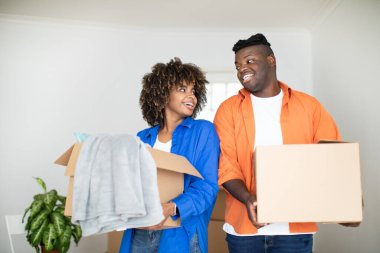 Taşınma Günü. Neşeli siyah eşler, ellerinde karton kutular, taşınırken Afrikalı Amerikalı çiftler, kendilerine ait eşleri taşıyorlar ve birbirlerine gülümsüyorlar, gayrimenkul alımını kutluyorlar.