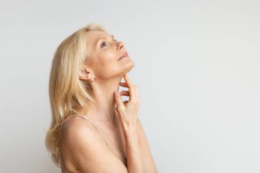 Esaslı bir güzellik. Yaşlı kadın yumuşak, pürüzsüz tenine dokunuyor, yaşlı bayan güzellik tedavisinin tadını çıkarıyor, arka planda duruyor, fotokopi çekiyor.