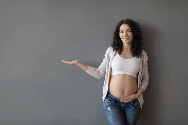 Usmívající Mladá Těhotná Žena Demonstrující Neviditelný Objekt Její Dlani Zatímco — Stock fotografie