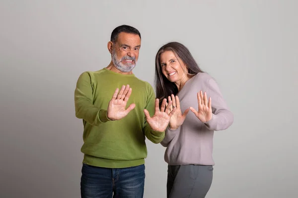 Sad dissatisfied caucasian elderly man and lady make stop gesture, disgust with hands on gray studio background. Bad offer, disappointed, forbidden, rejecting, personal space
