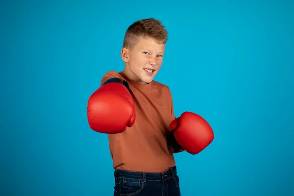 有趣的小男孩戴着拳击手套冲着相机冲着球 快乐的十几岁前男孩一边练习运动一边玩乐 在蓝色工作室的背景下孤立无援 复制空间 — 图库照片