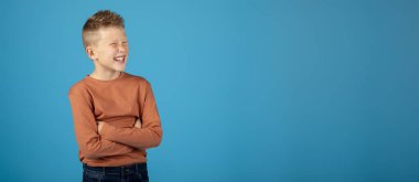 Fotokopi uzayına bakarken gözlerini kısarak bakan komik çocuk kollarını kavuşturmuş ve mavi stüdyo arka planında poz verirken burun kıvıran duygusal ergen çocuk Panorama