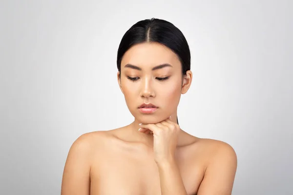 ダブルチン予防 明るい灰色の背景の上にアンチエイジングのスキンケア治療について彼女の顔の皮膚に触れるアジアの女性を動揺させます スキンケアの課題と美しさの欠陥 — ストック写真