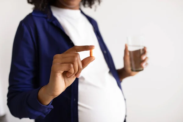 腹の大きいアフリカ系アメリカ人の妊婦は白い壁の背景の水のカプセルの丸薬 ガラスを示す 病気の治療 子供の期待のためのビタミン 母子保健医療 — ストック写真