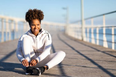 Gülümseyen genç siyah bayan atlet tahta iskelede oturuyor ve bağcıklarını bağlıyor mutlu, Afro-Amerikan sporcu kadın sabah koşusuna hazırlanıyor aktif Lyfestyle 'ın tadını çıkarıyor, Kopya Space