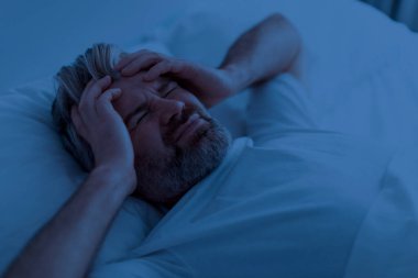 Mutsuz, orta yaşlı, sakallı, pijama giyen, başını okşayan, geceleri baş ağrısı çeken ve migren ağrısı çeken olgun bir adam.