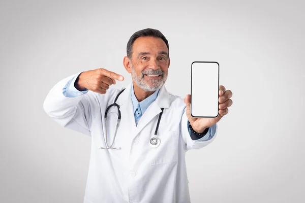 Glad European Mature Doctor White Coat Stethoscope Points Finger Smartphone — Stock Photo, Image