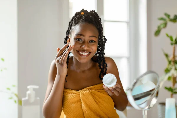肌の水分補給の純粋な喜び 自宅の寝室で鏡の前に座っている間 保湿クリームを適用する黒人女性を笑顔 美肌ルーチンを作る幸せな女性 — ストック写真