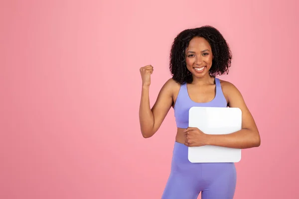 令人高兴的是 千年非洲裔美国女士穿着运动服 手持天秤 手握粉色背景的手拿着胜利标志 工作室 伟大的运动成果 饮食广告和提供 健身和身体护理 — 图库照片