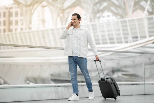 いつも連絡を取り合ってる 陽気な旅行者現代空港の屋内で旅行スーツケースを持って携帯電話で歩くことで フライトに出発する国際電話をかける男 ローミングオファー — ストック写真