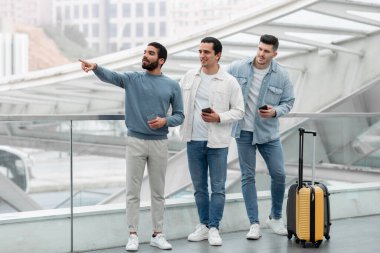 Gezici Seyahat Teklifi. Telefon kullanan üç turist, Modern Havalimanı 'nda Yeni İstikamet Pozisyonunu gösteren bir adam. Yolcu İletişimi