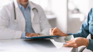 Sağlık sektörü yolsuzluk kavramı. Hasta el, doktor panosunun altına nakit para koyuyor. Klinik içi, yakın çekim.